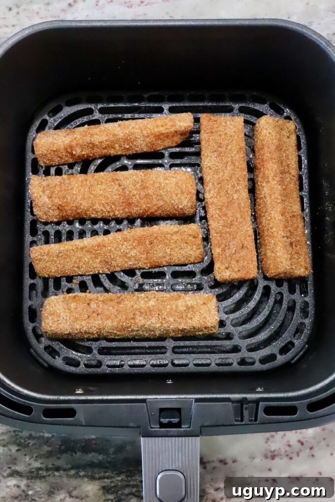 Six breaded fish sticks arranged in an air fryer basket on a kitchen counter. 