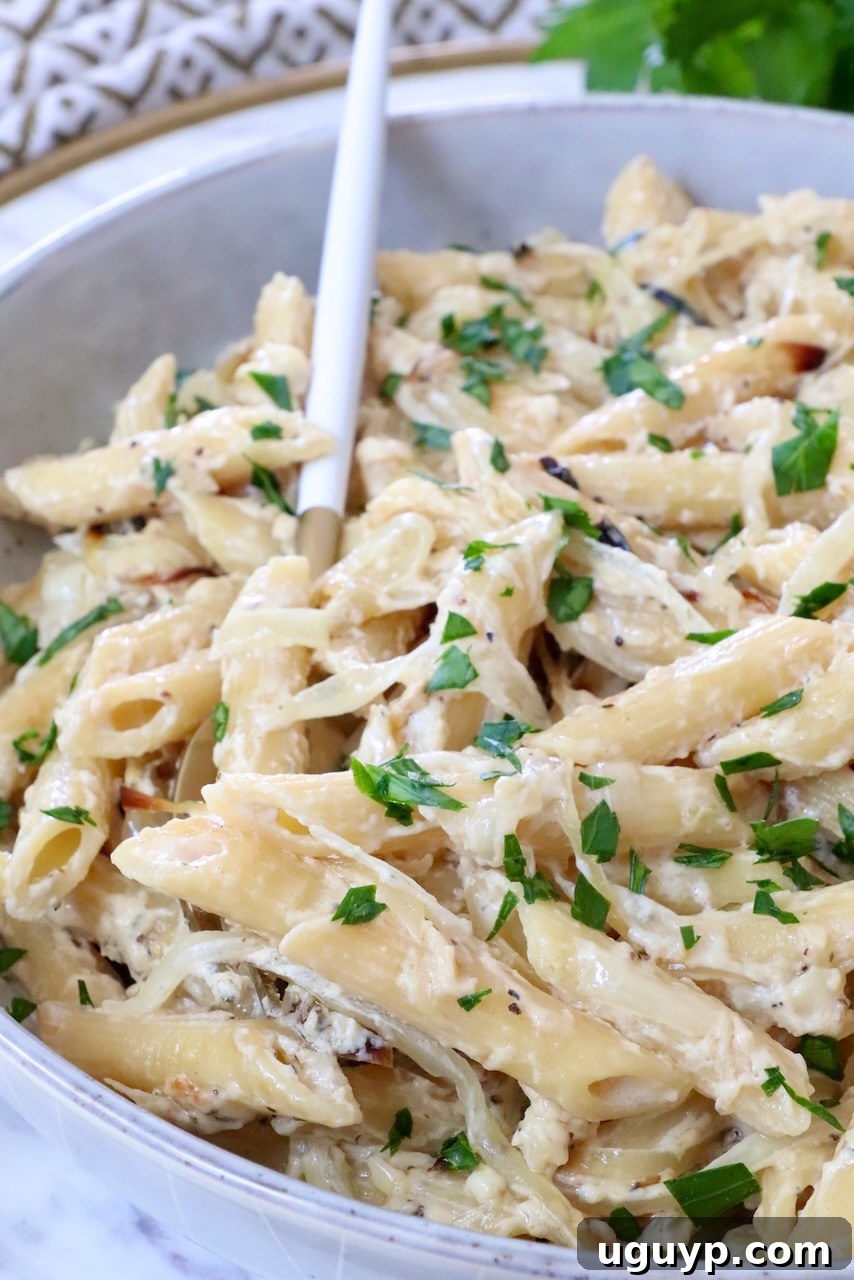 Creamy penne pasta topped with fresh parsley in a white bowl, accompanied by a white and gold spoon. 