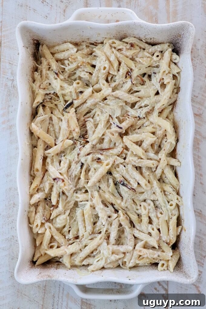 Creamy baked penne pasta in a white rectangular dish on a light wooden table.