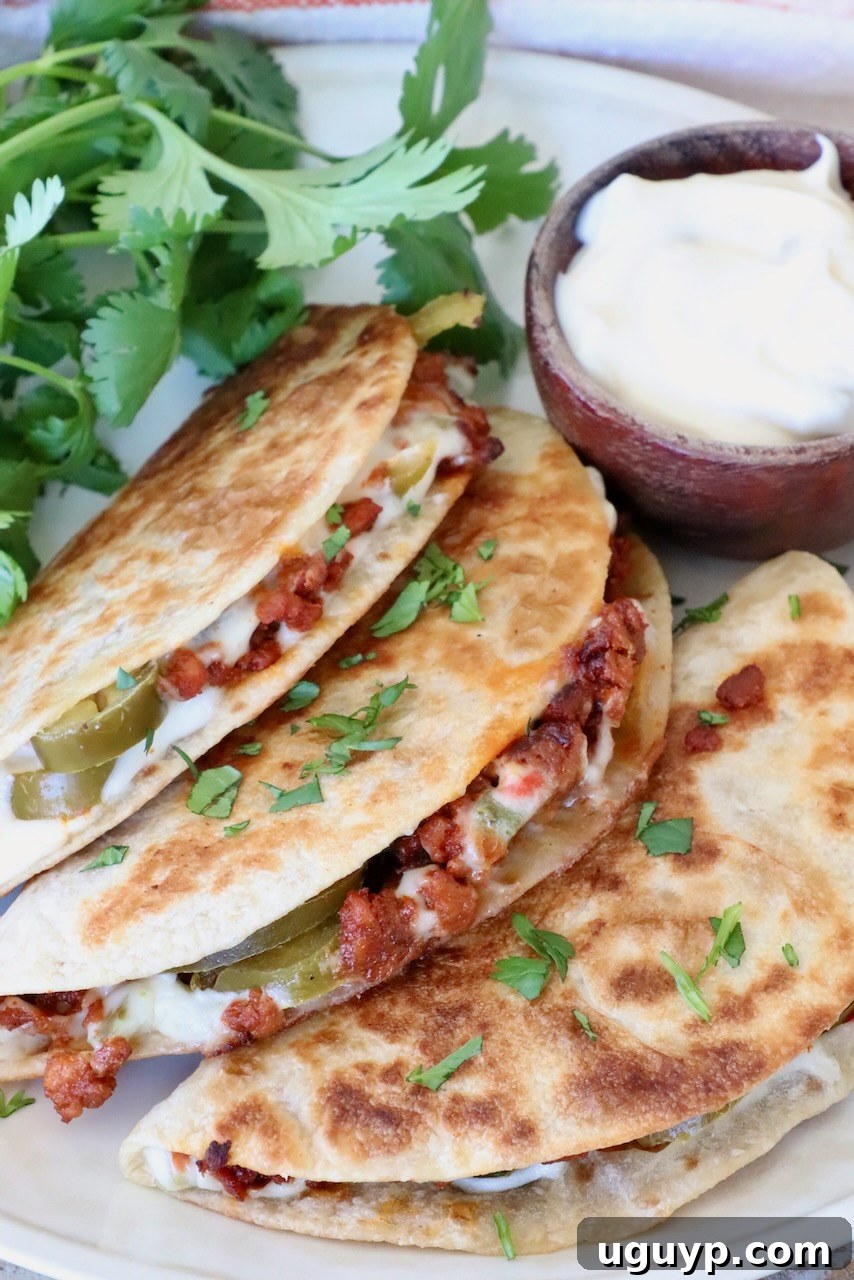 Three crispy tacos filled with succulent chorizo, rich white queso, and bright pickled jalapeños are artfully garnished with fresh cilantro. A small, inviting bowl of creamy white queso dip sits enticingly beside them on a rustic wooden surface.
