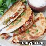 Three crispy tacos filled with chorizo, queso dip, and jalapeños are garnished with cilantro. A small bowl of white queso sits beside them on a plate.