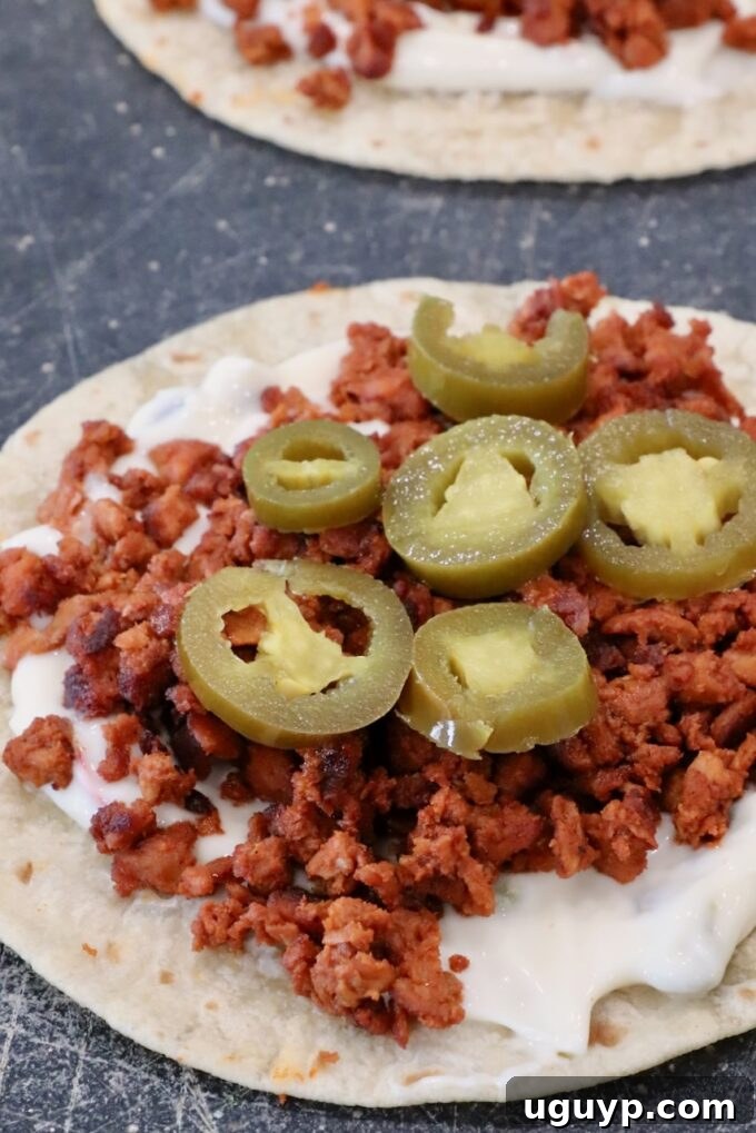 Close-up of an assembled taco filling: a warm tortilla layered with creamy queso dip, spicy crumbled chorizo, and vibrant sliced pickled jalapeños, ready to be folded.