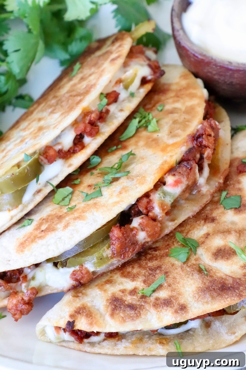 Three perfectly crispy tacos, brimming with spicy chorizo, creamy cheese, and zesty jalapeños, are delicately garnished with fresh cilantro. A small bowl of luscious white queso dip sits nearby, inviting you to dip.