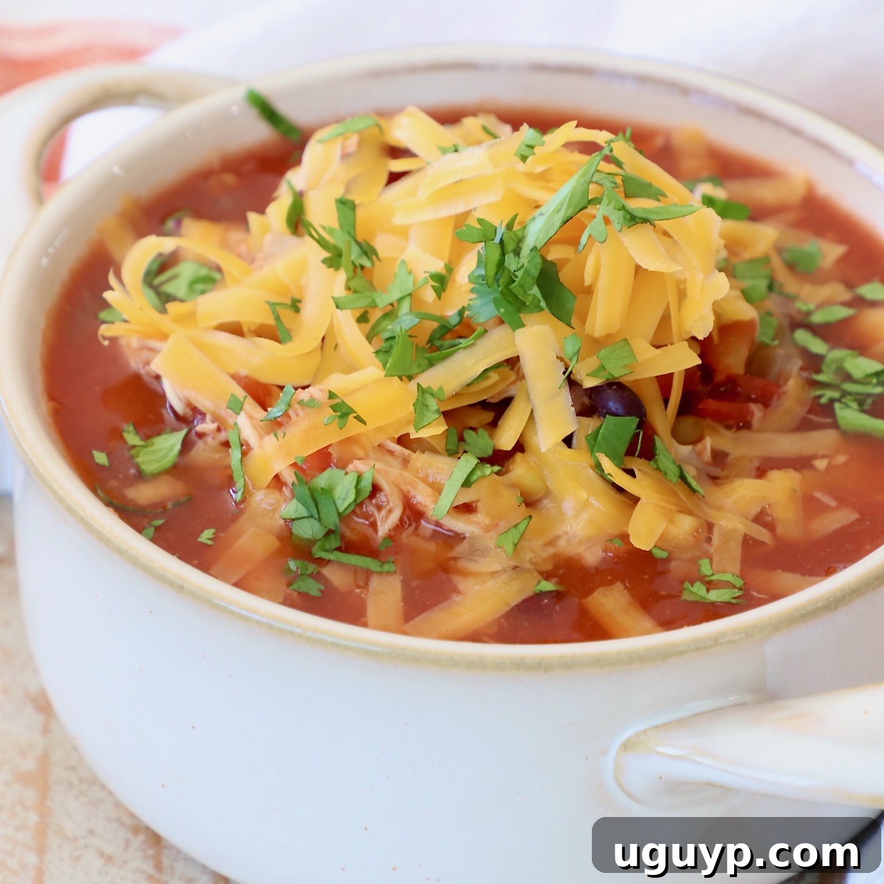 Slow Cooker Chicken Enchilada Soup in a white crock, topped with melted cheddar cheese.