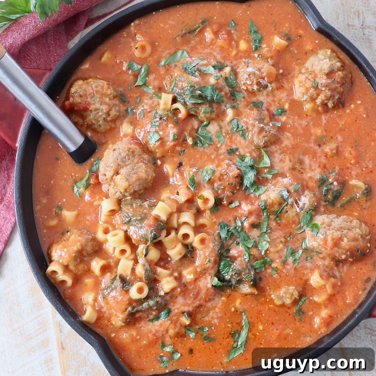 Hearty Italian Meatball Soup in a skillet, ready to serve with a spoon. Packed with homemade meatballs, pasta, and a creamy tomato broth.