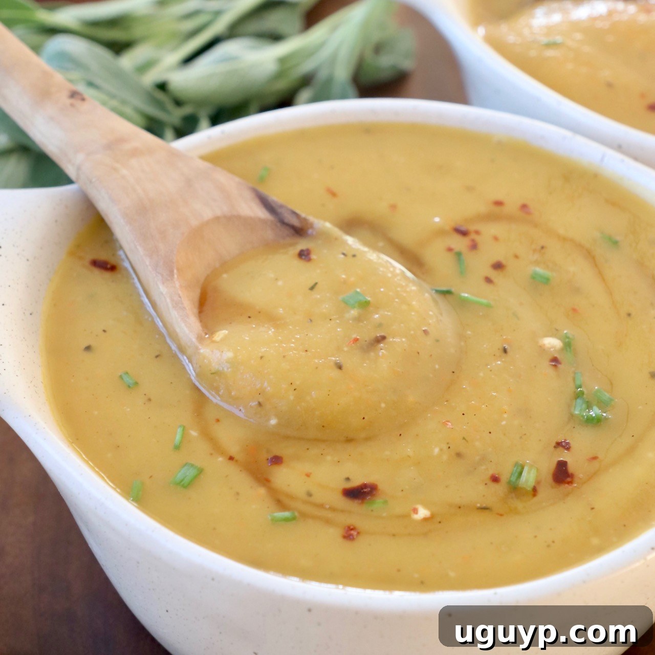 Creamy Acorn Squash Soup in a bowl with a wooden spoon, garnished and ready to serve.