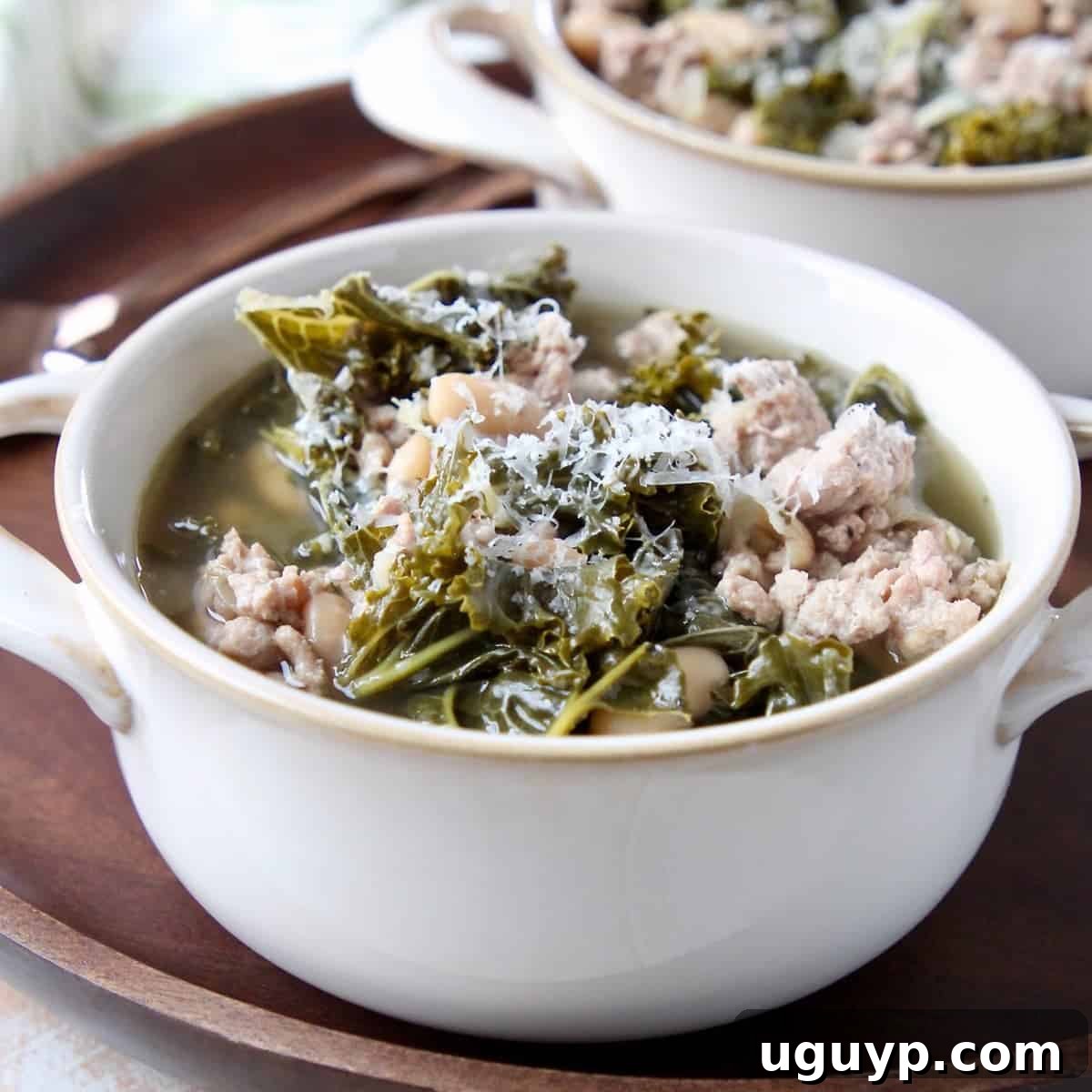 Hearty Kale Turkey Soup in a white soup crock on a dark wood tray, ready to be served.