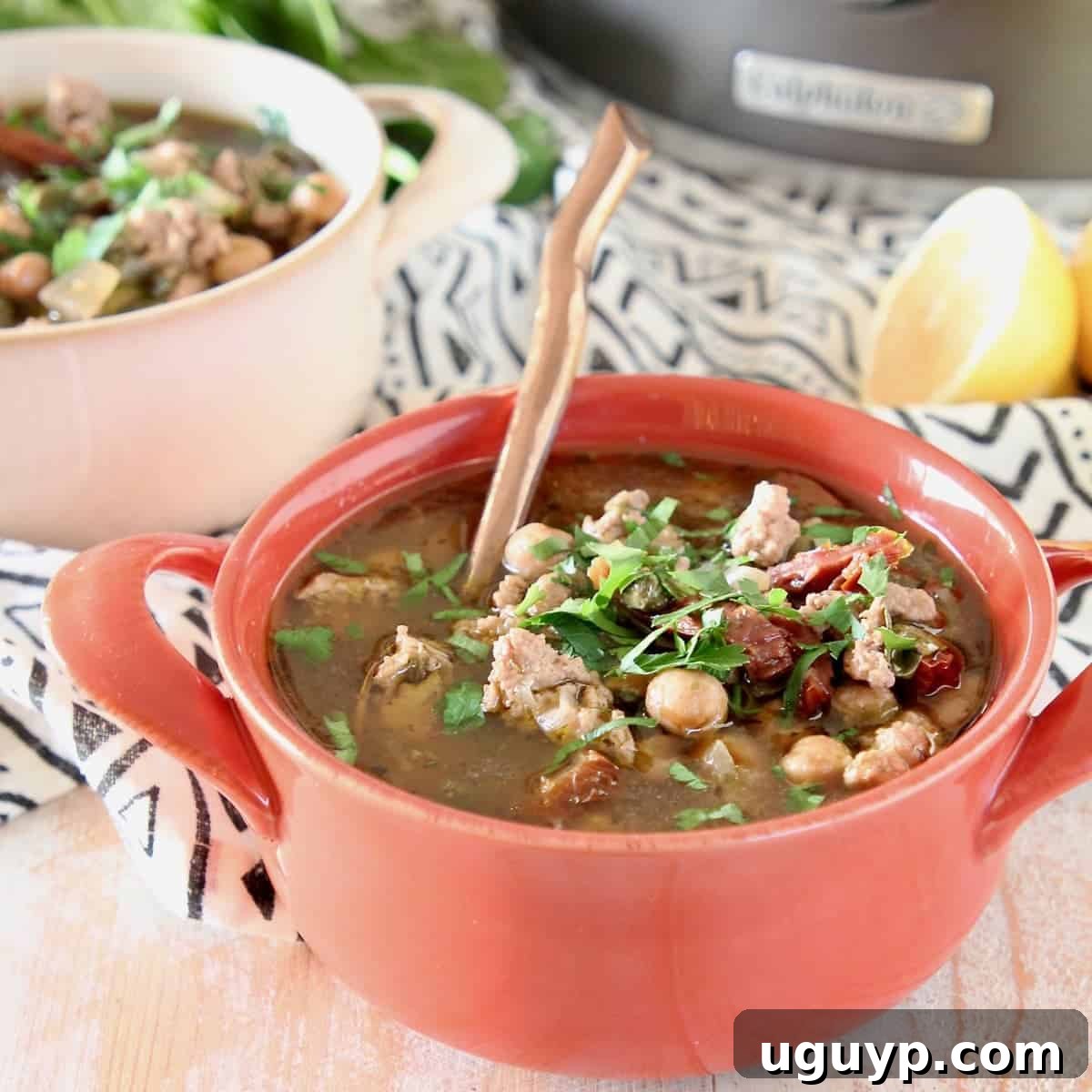 Healthy Greek Turkey Soup with chickpeas and spinach in an orange bowl, garnished with a slice of lemon.