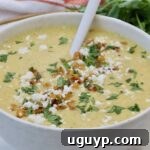 A creamy corn soup topped with crumbled cheese, cilantro, and golden corn kernels fills a white bowl.