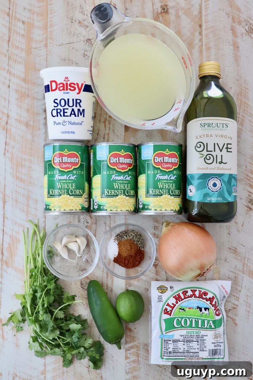 A beautifully arranged flat lay of fresh ingredients for Mexican Street Corn Soup, showcasing canned corn, sweet onion, vibrant jalapeño, aromatic garlic cloves, fresh cilantro, bright lime, creamy sour cream, crumbly cotija cheese, olive oil, and a selection of smoky spices on a rustic wooden background.