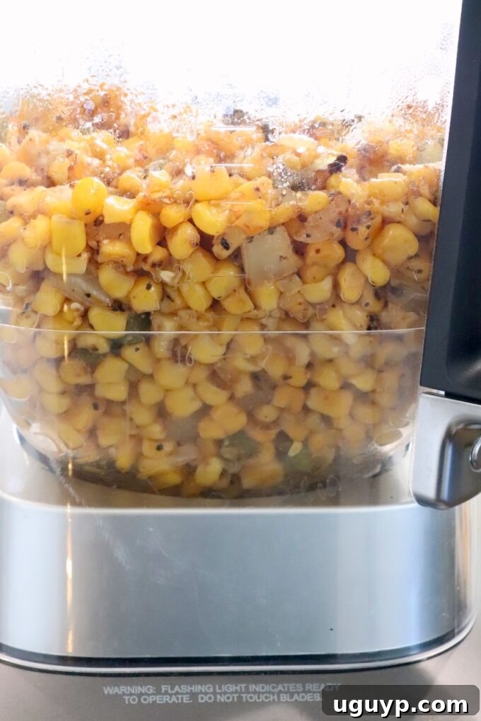 Roasted corn, onions, jalapeños, and tender garlic cloves are scooped into a blender, forming the base for the creamy soup, ready to be pureed with other liquid ingredients.