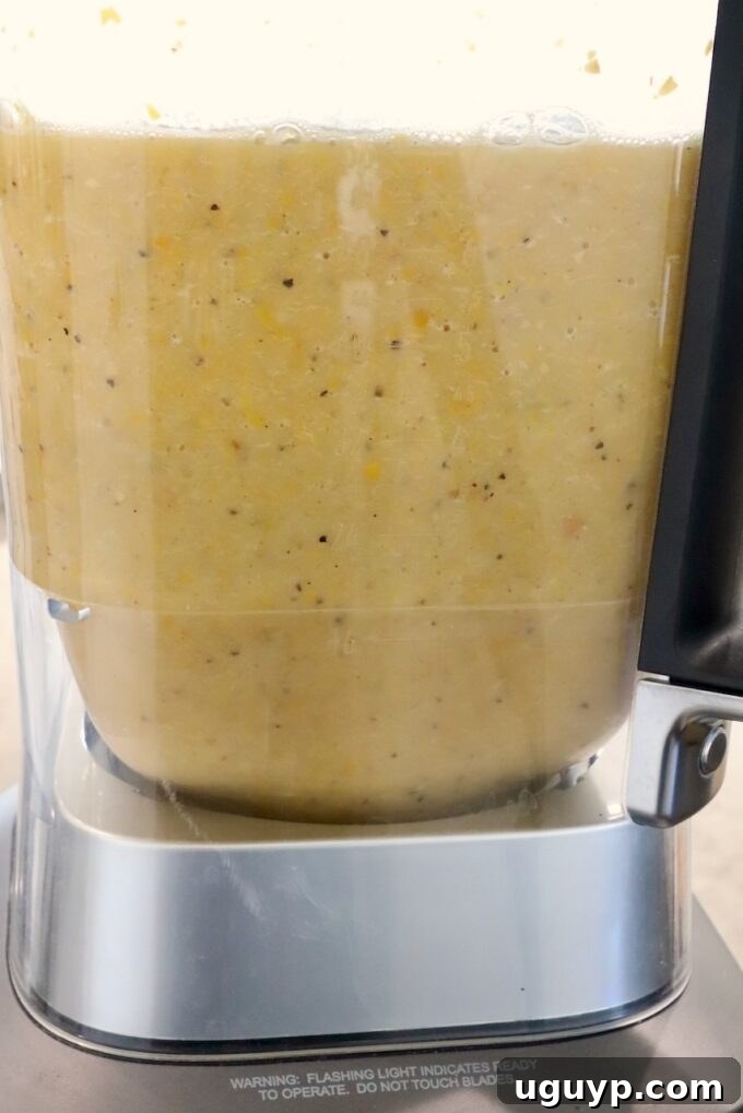 The creamy, pureed Mexican Street Corn Soup swirls beautifully inside a blender, showcasing its smooth texture after processing the roasted vegetables and liquids, indicating it's almost ready.