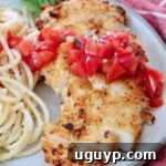 crispy chicken sliced on a plate topped with tomato bruschetta with creamy pasta noodles on the side