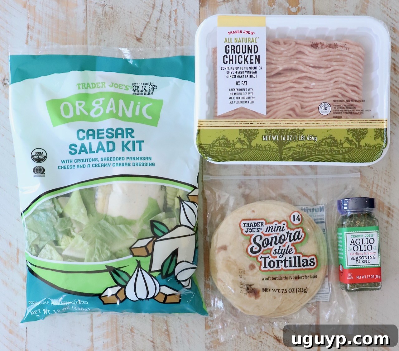 Four key ingredients for Chicken Caesar Smash Tacos are neatly arranged on a rustic wooden surface: a package of organic ground chicken, a bottle of Aglio Olio seasoning blend, a stack of mini Sonora tortillas, and a Trader Joe’s Caesar salad kit.