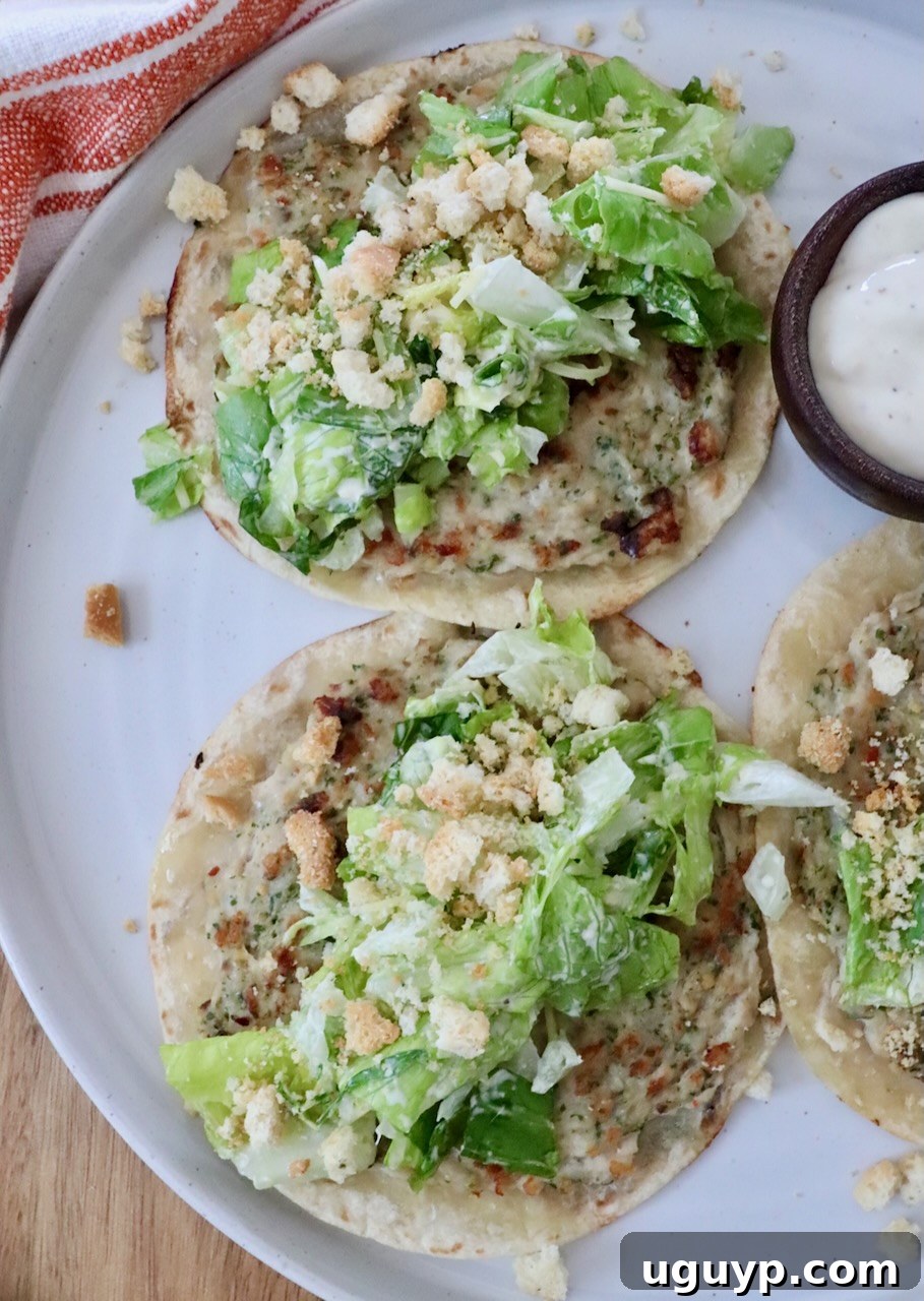 Three perfectly assembled mini Chicken Caesar Smash Tacos, featuring crispy chicken-smashed tortillas topped with vibrant romaine lettuce, crumbled croutons, and a drizzle of creamy Caesar dressing, elegantly presented on a white plate. A small bowl of extra dressing is ready on the side.