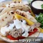 Grilled steak with yellow and red bell peppers, topped with creamy white queso in charred tortillas. Garnished with fresh cilantro on the side and a cup of queso on the side.