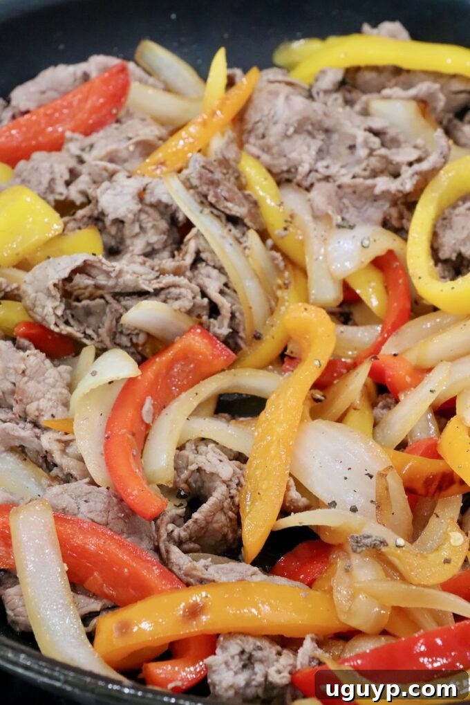 cooked steak, bell peppers, and onions in a skillet