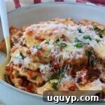 Close-up of a bowl of baked ravioli with melted cheese, garnished with fresh herbs with a fork in the bowl. Behind it, a red-striped cloth.
