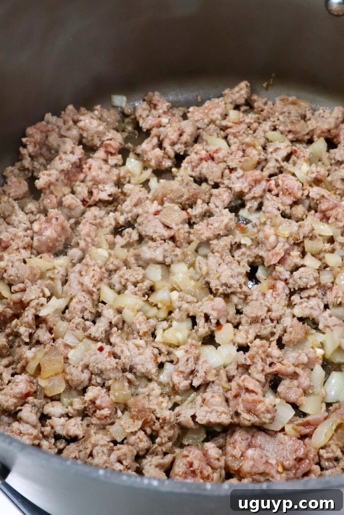 Ground Italian sausage browning in a large skillet with diced onions, creating a fragrant base for the meat sauce.