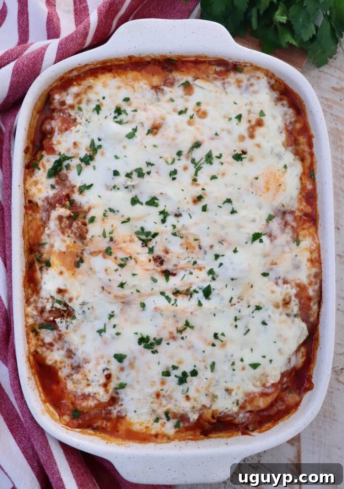 The finished cheesy baked ravioli casserole, golden and bubbling from the oven, garnished with fresh basil leaves, next to a red-striped towel and more fresh herbs.