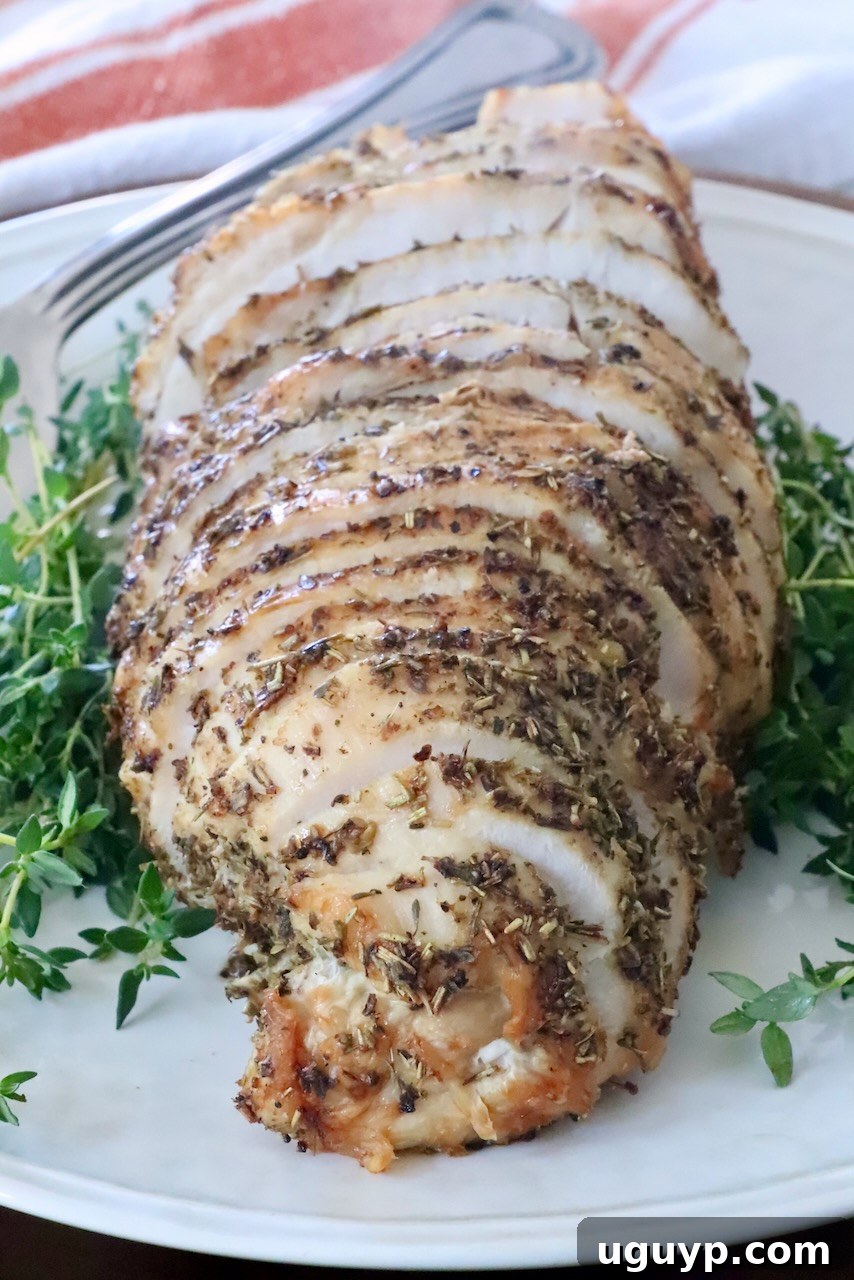 Sliced herb-crusted roast turkey breast on a white plate, surrounded by fresh green herbs.