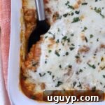 Close-up of butternut squash baked ravioli in a white dish. It features a golden-brown cheese topping sprinkled with herbs, with a serving spatula on the side.