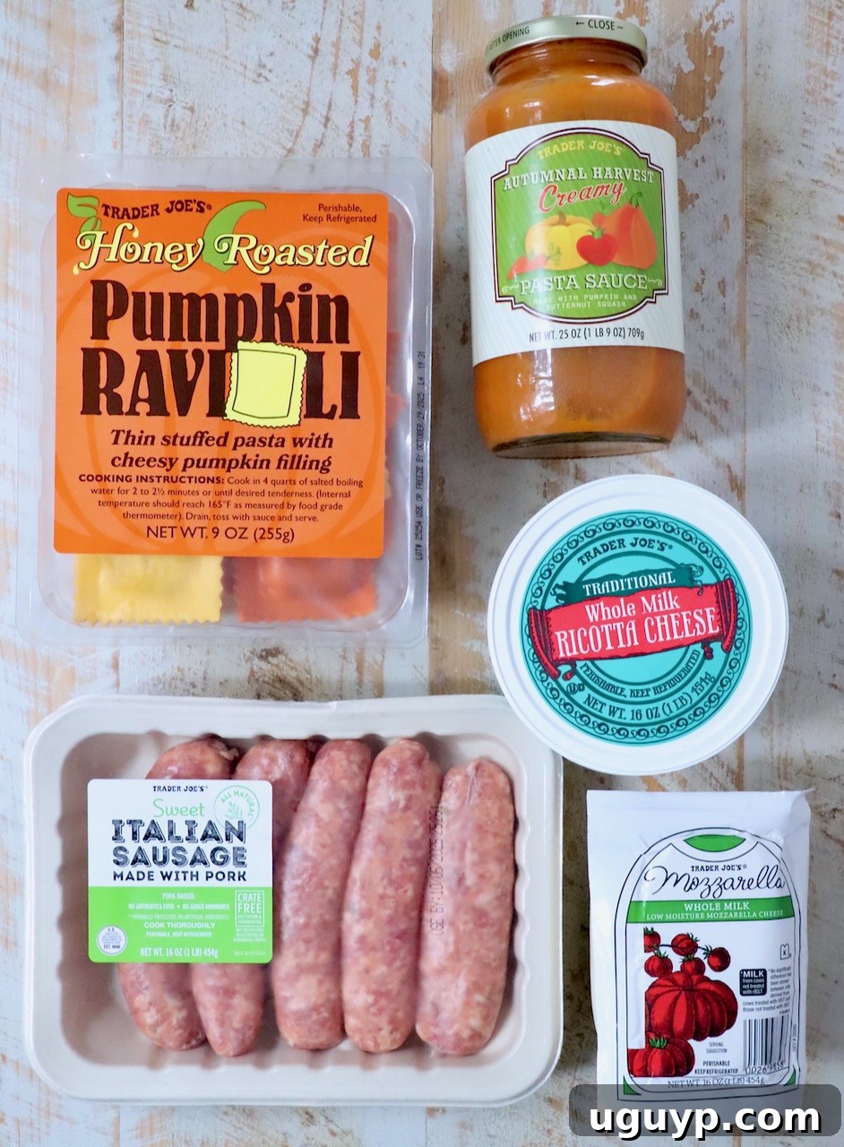 Key Trader Joe's ingredients for the recipe laid out on a rustic wooden surface: Honey Roasted Pumpkin Ravioli, Autumnal Harvest Pasta Sauce, Sweet Italian Sausage, Ricotta Cheese, and a block of Mozzarella.