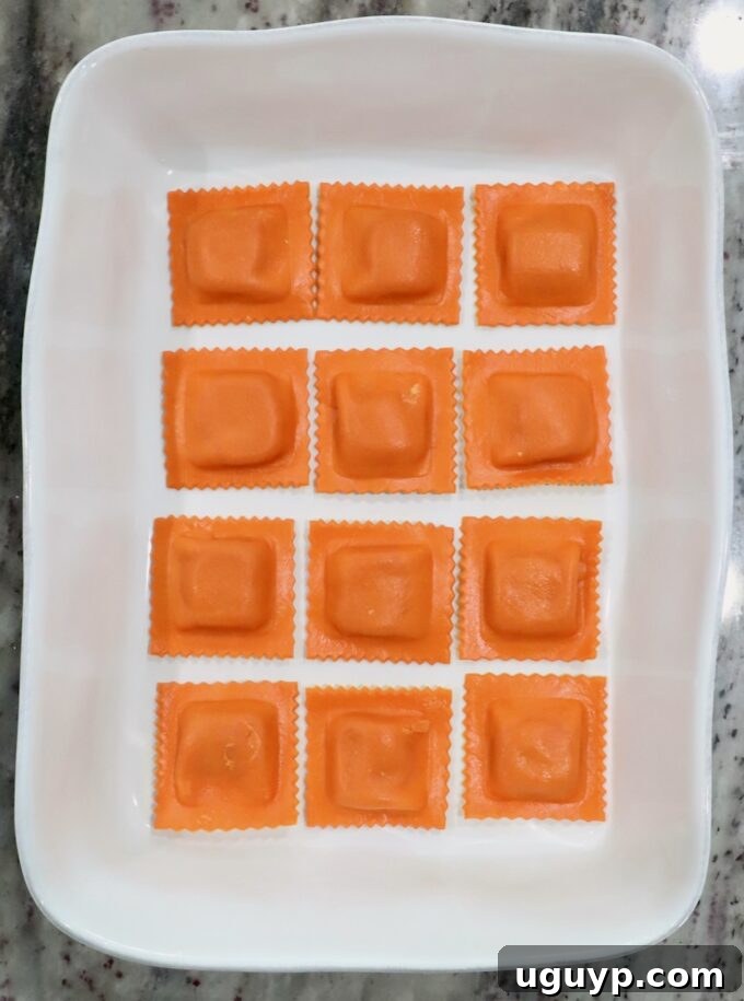 Twelve pumpkin ravioli arranged neatly in a rectangular white dish on a marble countertop