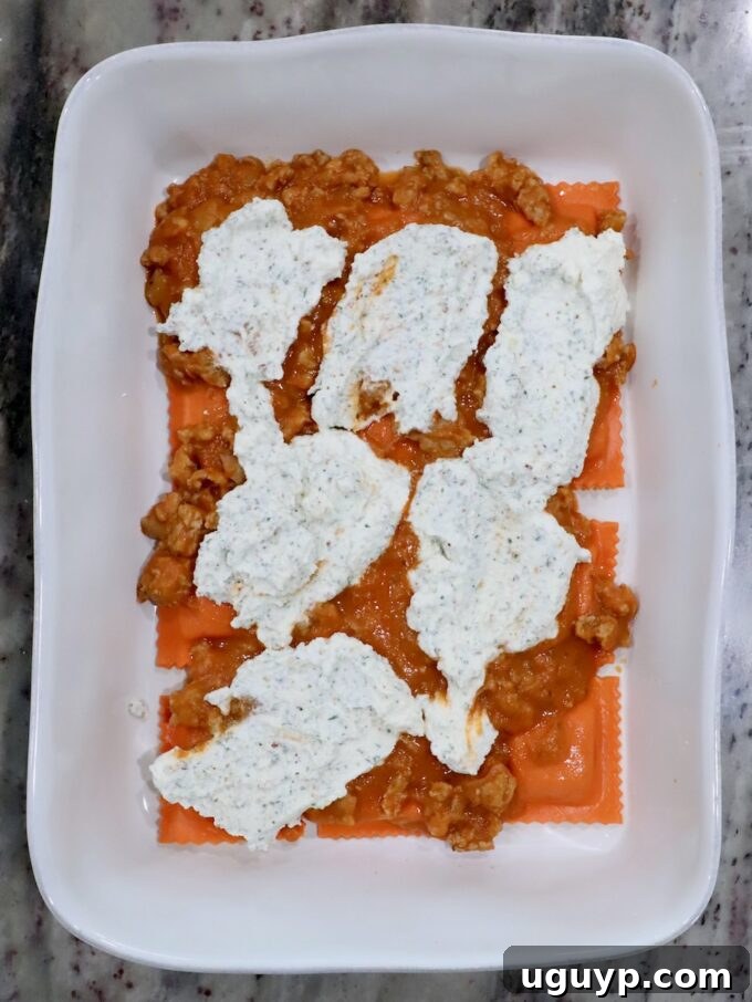 pumpkin ravioli in a baking dish, topped with butternut squash meat sauce and seasoned ricotta cheese