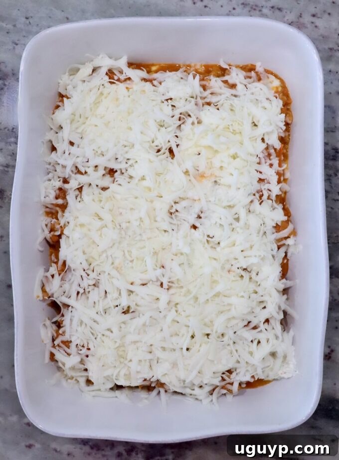 White rectangular baking dish filled with layered pumpkin ravioli, topped with shredded mozzarella cheese. 