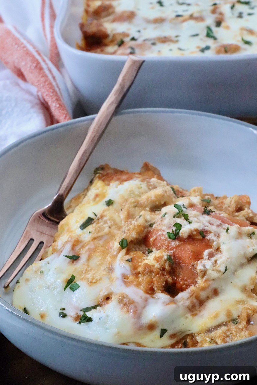A close-up of a creamy, cheesy pasta bake in a bowl with a fork, garnished with fresh herbs. In the background, a baking dish of the same pasta, ready to be served.