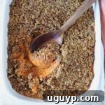 Close-up of a sweet potato casserole with a crunchy pecan topping and a wooden spoon scooping the orange sweet potato filling out from the dish