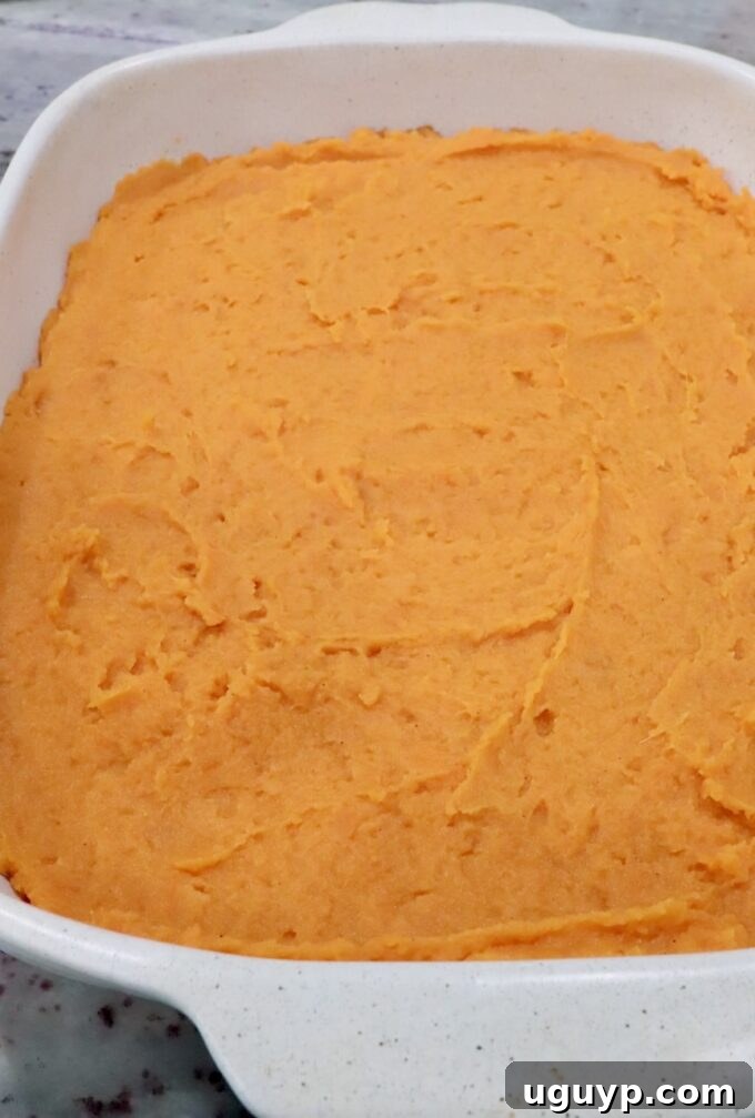 Creamy orange mashed potatoes in a white square dish, spread evenly. 