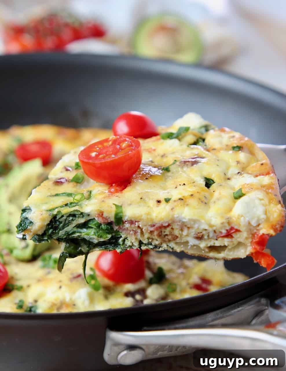 A perfectly cooked slice of spinach frittata with bacon and goat cheese, ready to be served from a skillet.