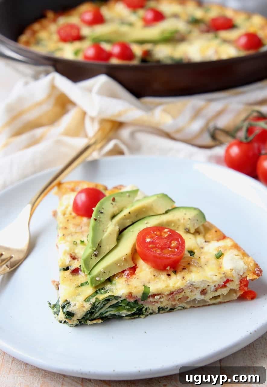 A delectable slice of spinach frittata with goat cheese and bacon on a plate, accompanied by a fork.