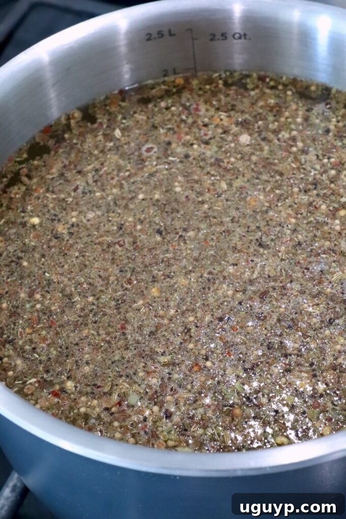 A shimmering silver pot brimming with a flavorful simmering liquid, infused with a medley of whole spices and seeds, creating an aromatic brine.