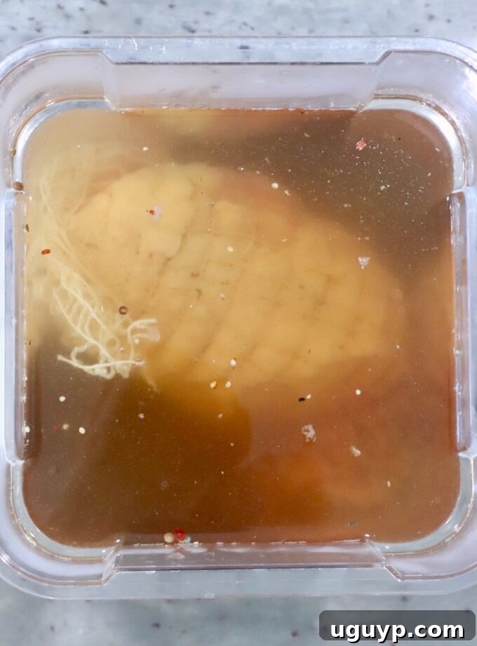 A pristine boneless turkey breast submerged in a light amber-colored brine, meticulously contained within a clear plastic storage vessel, ready for its flavor infusion.