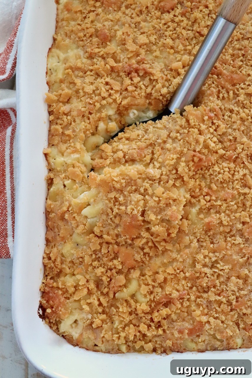 Golden-brown baked macaroni and cheese with a crispy cracker topping in a white casserole dish. A serving spoon is lifting a portion, revealing creamy pasta underneath.