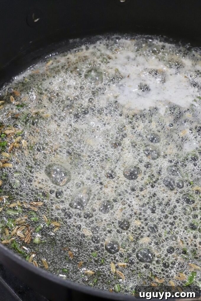 Close-up of seeds and herbs simmering in a bubbling, frothy liquid in a black pot