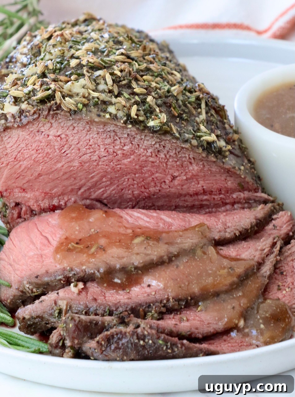 Herb-crusted roast beef, thinly sliced and served on a white plate with brown gravy drizzled over the slices of beef.