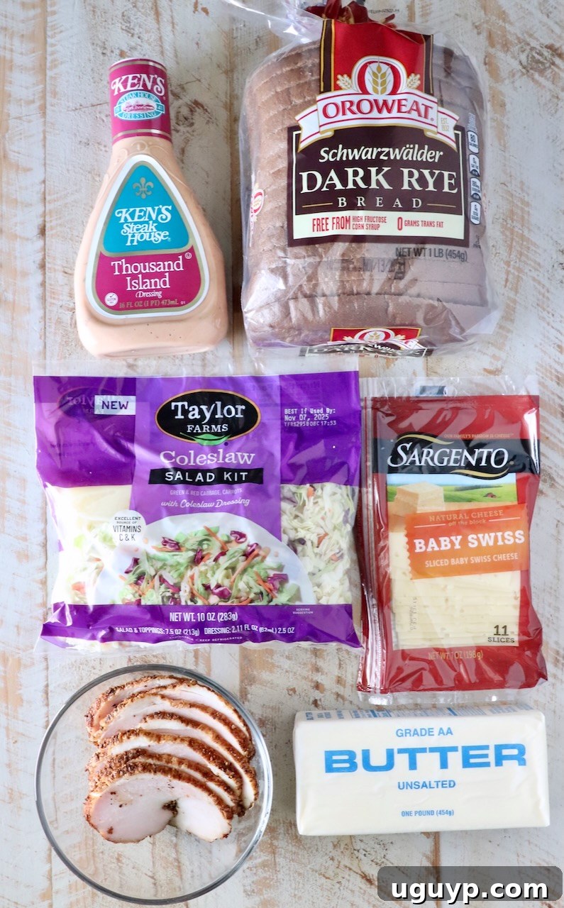 Packaged ingredients on a wooden table include Thousand Island dressing, dark rye bread, coleslaw kit, baby Swiss cheese, sliced cooked turkey, and butter.