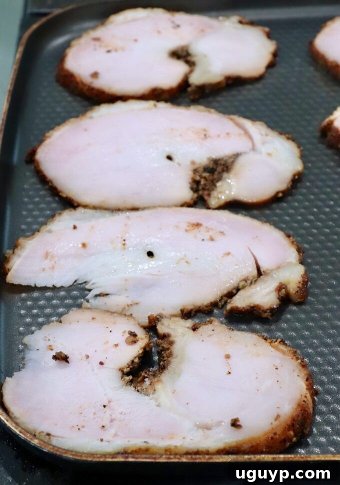Slices of roasted turkey breast with a browned seasoning crust are laid out on a textured skillet.