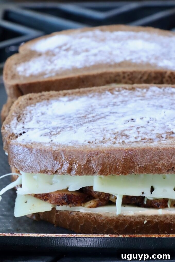 Two sandwiches on a stove. The bread is buttered, with melted cheese and grilled meat peeking out.