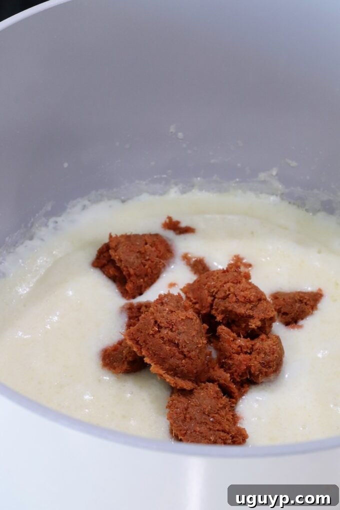 creamy roux sauce in a pot topped with spoonfuls of red curry paste