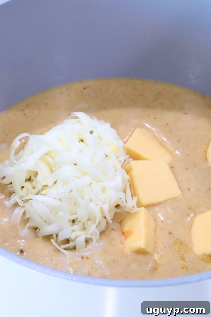 creamy red curry sauce in a pot with cubed Velveeta cheese and shredded pepper jack cheese