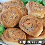 Close-up of savory swirled pastry rolls with a golden, crispy crust. Filled with sausage and tomatoes, garnished with fresh cilantro, on a white plate.