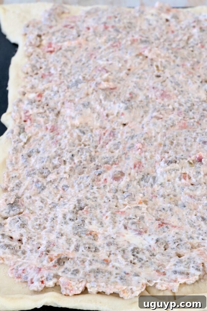 crescent roll dough covered in a cream cheese sausage mixture on a cutting board
