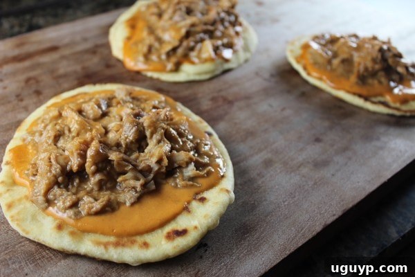 Assembled pizzas on roti bread with peanut sauce and pulled pork, ready for grilling.