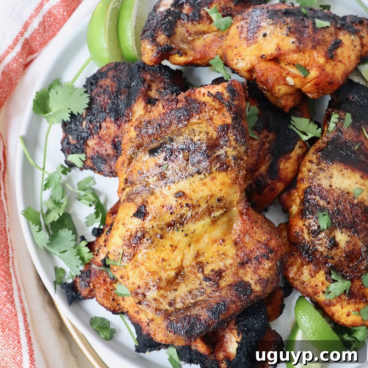 grilled chicken thighs stacked up on a plate with fresh cilantro and lime wedges