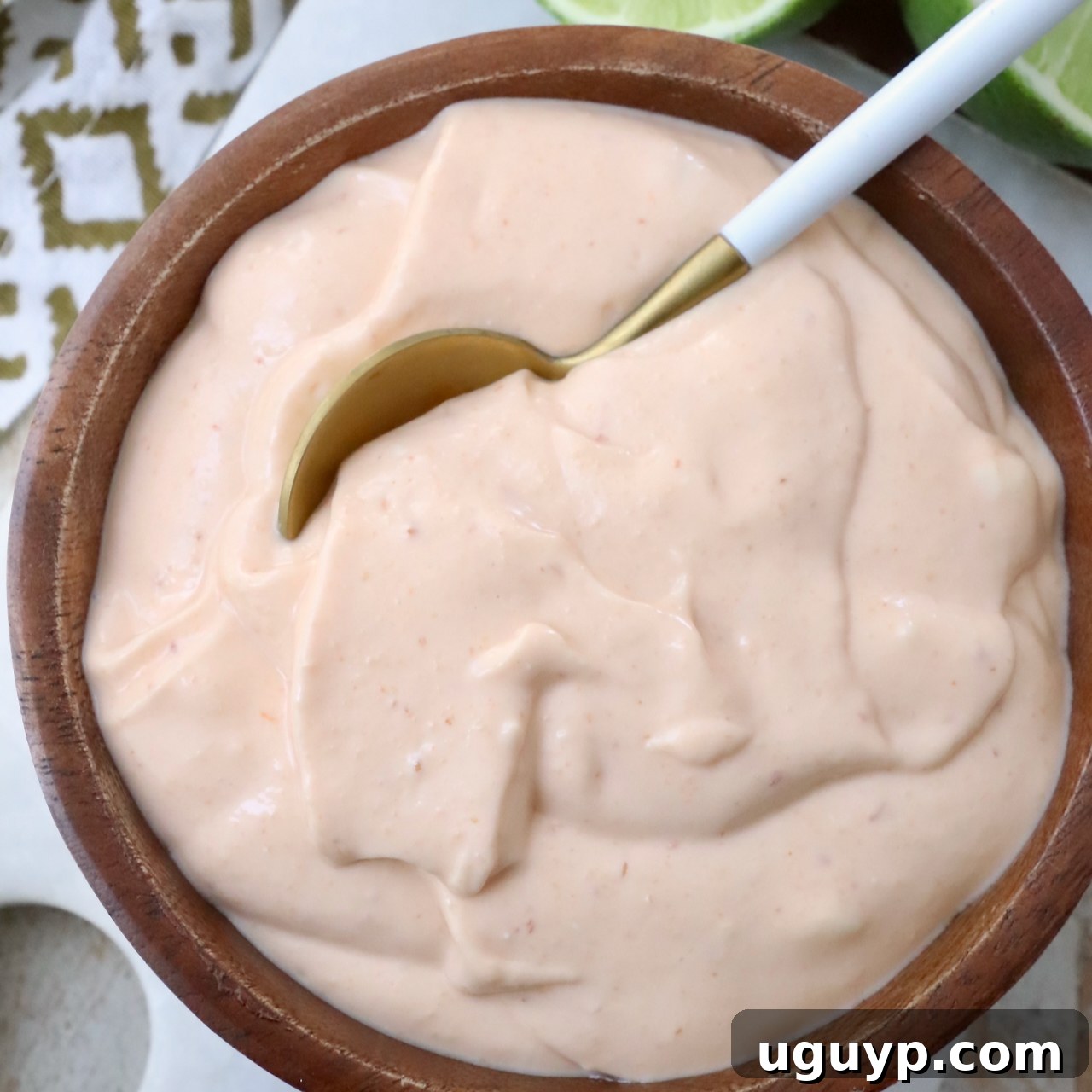 A wooden bowl filled with creamy, light orange sauce. A spoon dips into the smooth mixture.